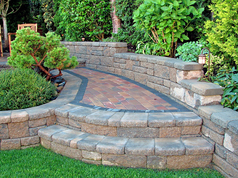 A close-up view of stone steps with following footpath and deck area incorporated into a low retaining wall part of a garden landscape design.